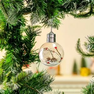 Dettaglio pallina di Natale trasparente con bacche rosse e pigne appesa a un pino