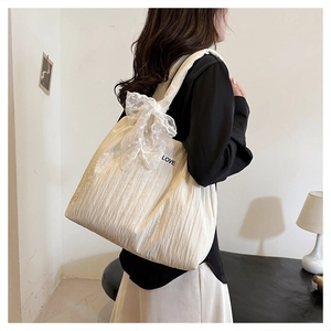 Detail of cream tote bag featuring pleated fabric texture and lace bow with LOVE patch