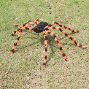 Gran araña de peluche de Halloween con patas rayadas naranja sobre césped en exteriores
