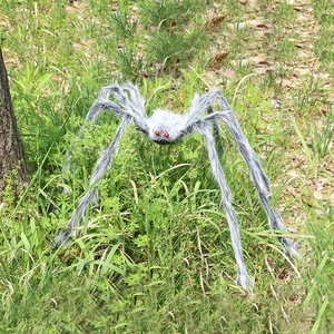 Close-up of a large grey plush spider with red eyes on green grass for Halloween decor