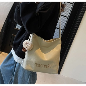 Detail of off-white tote bag featuring Summer embroidery and a plush doll pendant