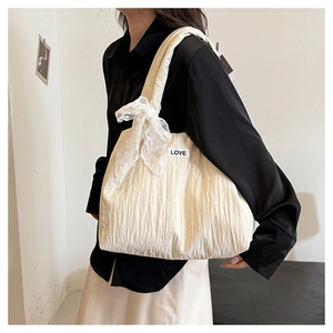 Detail of white tote bag featuring pleated texture, lace bow, and LOVE label on shoulder