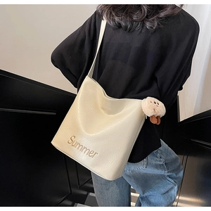 Detail of off-white tote bag featuring golden Summer embroidery and a plush bear charm