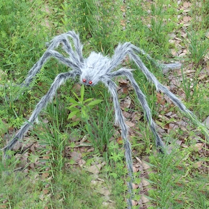 Giant Halloween spider decoration with grey plush fur and red eyes on autumn lawn