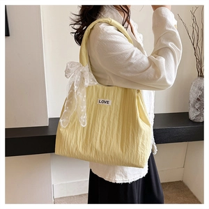 Detail of yellow pleated tote bag with white lace bow and LOVE patch on person