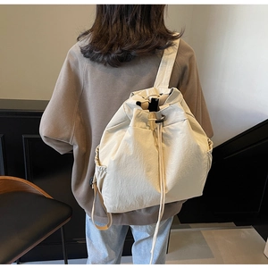 Détail du sac à dos beige à cordon montrant les poches latérales et la sangle sur un modèle