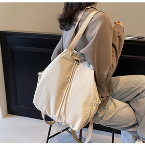 Vue latérale du sac à dos beige à cordon sur mannequin montrant le design seau et la poche