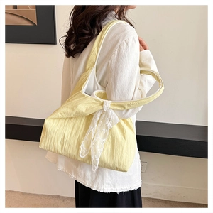 Detail of yellow pleated tote bag featuring a decorative white lace bow on the strap