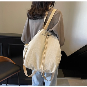 Détail du sac à dos en toile crème avec cordon de serrage et poches latérales pratiques