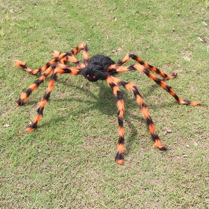 Araña gigante de Halloween con felpa negra y patas de rayas naranjas en el césped