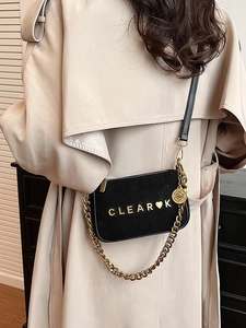 Matte black crossbody bag with gold chain and CLEAR lettering on a beige trench coat