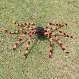 Araña gigante de peluche para Halloween con rayas naranjas en césped de jardín