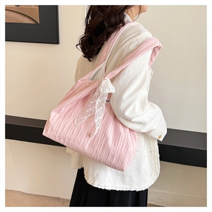 Detail of pink pleated tote bag featuring a delicate white lace bow and textured fabric