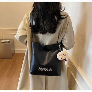 Detail of black leather tote bag with Summer embroidery and plush charm on white coat
