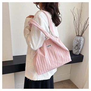 Detail view of a pink pleated tote bag with LOVE patch on a minimalist interior background
