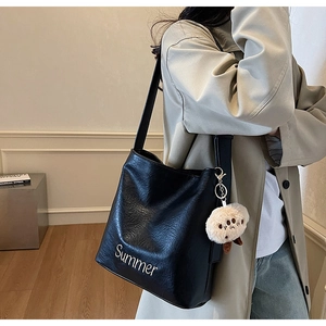Detail of black leather bucket bag featuring white Summer embroidery and plush doll charm