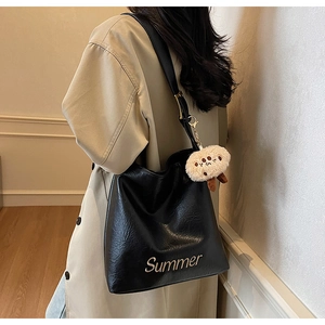 Detail of a black glossy leather tote bag with a gold Summer logo and a plush bear charm