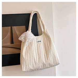 Detail of cream pleated tote bag featuring delicate lace bow and black LOVE label