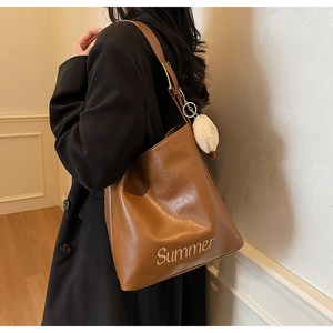 Close-up of brown textured tote bag with Summer embroidery and white plush charm