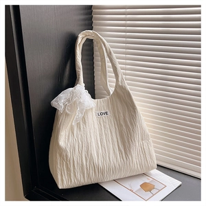 Close-up of pleated cream tote bag featuring a LOVE label and lace bow accessory