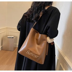 Detail of caramel brown tote bag featuring white Summer embroidery and plush charm accessory