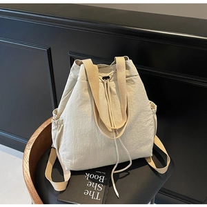 Vue détaillée du sac à dos crème avec cordon et sangles camel sur une chaise noire