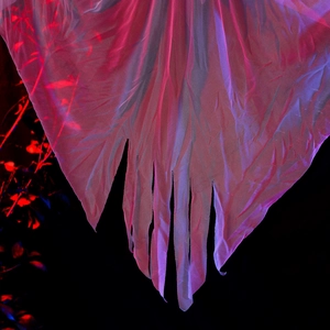 Detail of tattered translucent white mesh fabric with eerie neon pink and red lighting