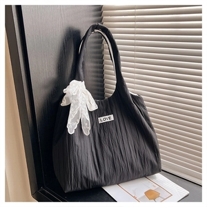 Detail of black pleated tote bag featuring LOVE patch and white lace bow decoration