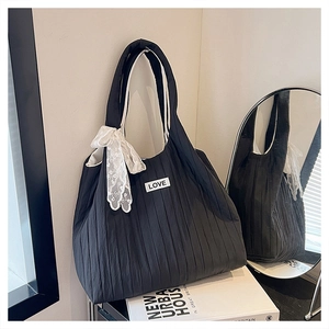 Detail of black pleated tote bag with white bow pendant and LOVE label in lifestyle setting