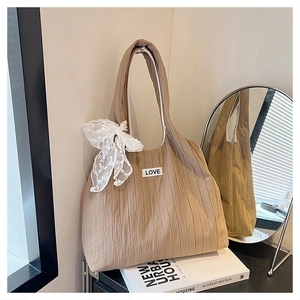 Close-up of beige pleated tote bag featuring a white lace bow and LOVE patch detail