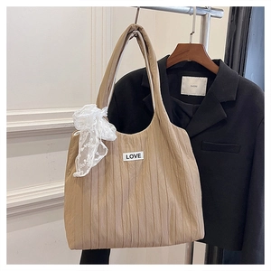 Detail of khaki pleated tote bag with lace bow and LOVE patch on a black blazer