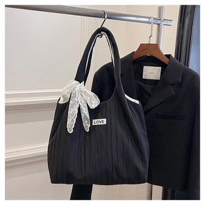 Detail of black pleated tote bag with white LOVE patch and decorative lace ribbon bow