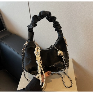Detail of black pleated cloud bag with golden chain strap and braided charm