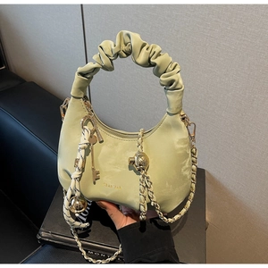 Detail of mint green ruched handbag showing gold chain and key pendant on a black book