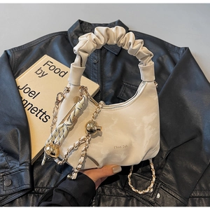 Detail of cream hobo bag with pleated handle and golden chain on black leather background