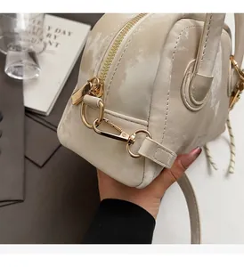 Close-up of premium gold-tone hardware and pearlescent textured leather on off-white handbag