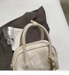 Detailed view of cream textured handbag featuring double handles and woven tassel charm