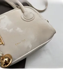 Detail of beige suede handbag showing golden brand logo and premium metal hardware