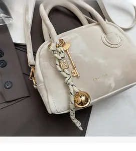 Close-up of off-white leather handbag with gold key and woven rope charms on a blazer