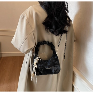 Detail of black pleated handbag with metal chain and branded lettering on beige trench coat