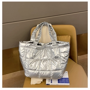 Close-up of metallic silver quilted puffer tote bag with ruched handles on a soft chair