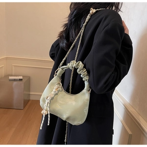 Detail of light green pleated leather bag with gold chain and woven charm on model