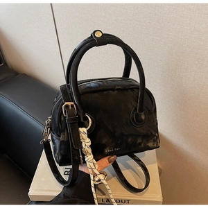 Detail view of glossy black Boston bag with top handles and braided rope charm accessory