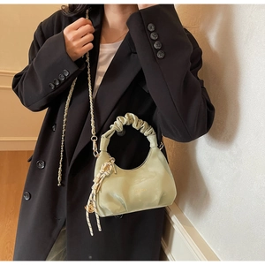 Detail of pistachio green pleated cloud bag with elegant chain strap and knotted charm