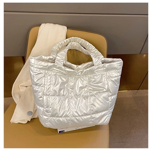 Detail of white quilted down tote bag with metallic finish on a yellow chair