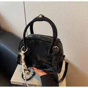 Detail of glossy black Boston bag with gold zipper and woven bell charm accessory
