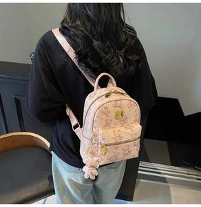 Roze mini-rugzak met teddybeerprints en gouden logoplaat gedragen door een model