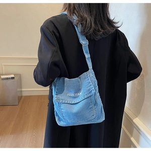 Détail d'un sac bandoulière en denim bleu clair avec broderie blanche et sangle réglable