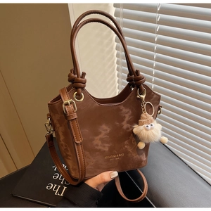 Detail of a brown oil wax leather tote bag featuring a ring handle and plush charm