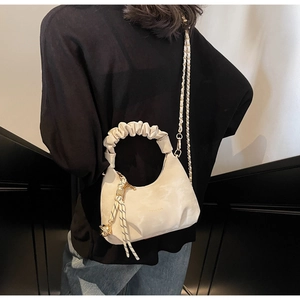 Detailed view of cream pleated cloud bag featuring gold chain and spherical metal charm